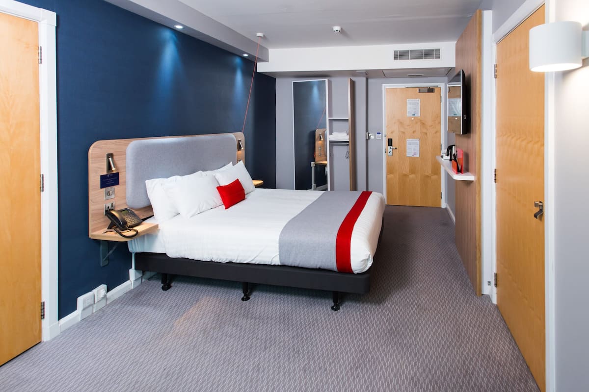 A hotel room with a bed, bedside table, phone, and a mirror.