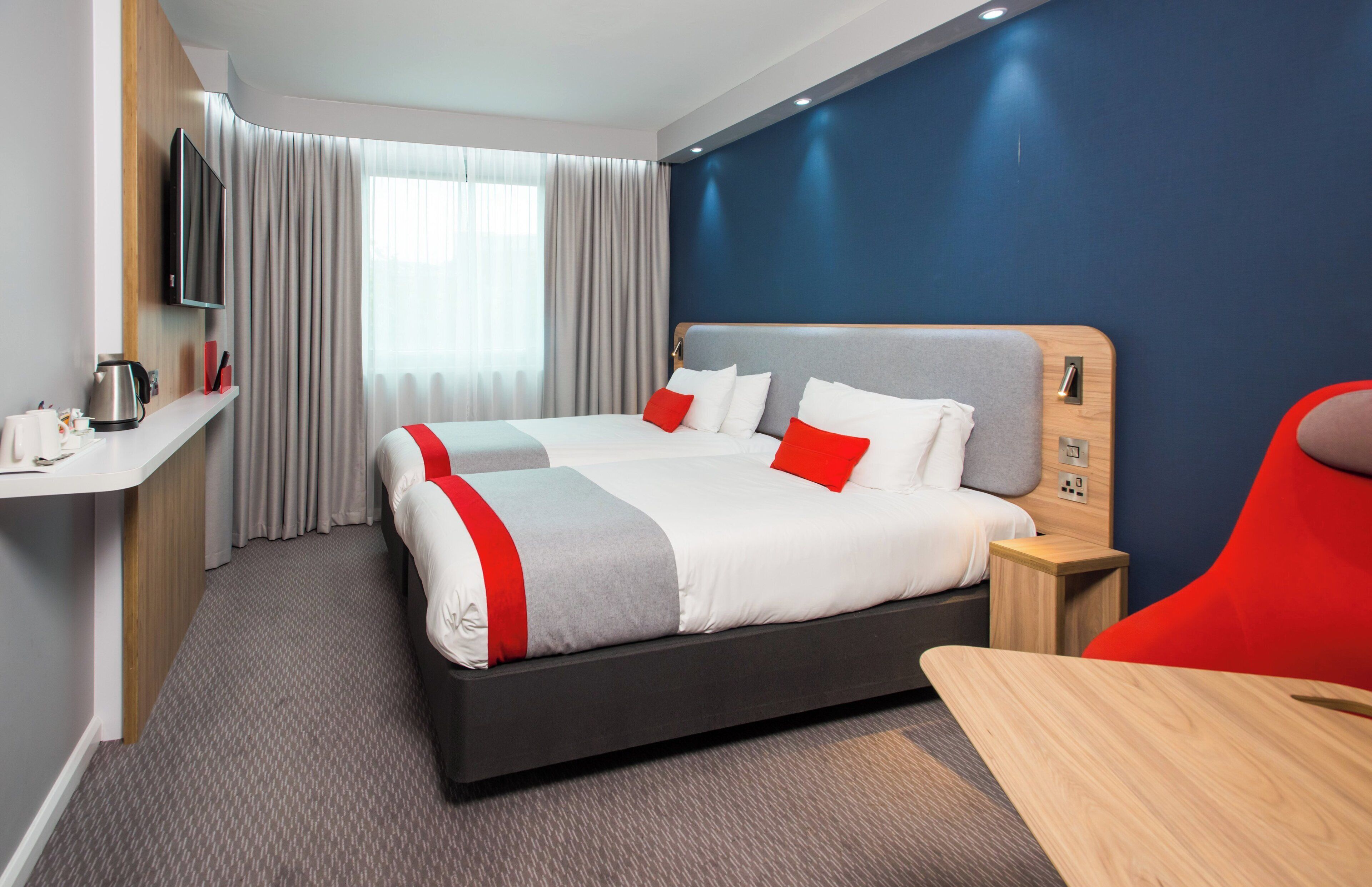 Een moderne hotelkamer met een bed, nachtkastje en een rode stoel.