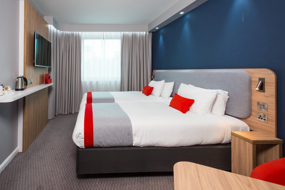 A modern hotel room with a large bed, a TV mounted on the wall, a bedside table, and a window with curtains.