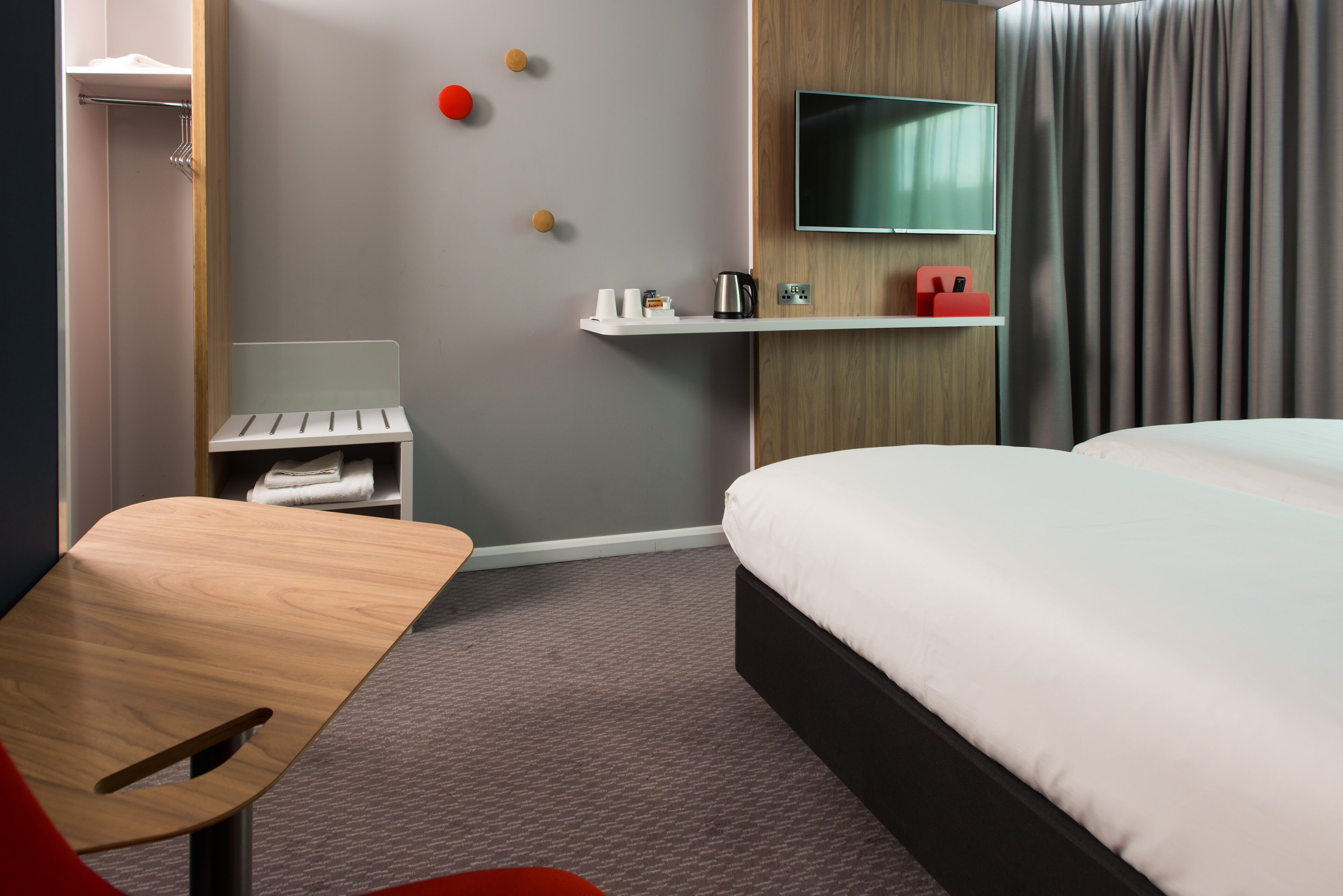 A modern hotel room with a bed, a desk, a TV, and a shelf with toiletries.
