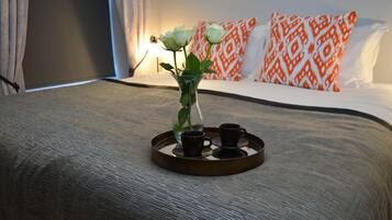 Un lit bien fait, sur lequel repose un plateau avec un vase contenant une fleur et deux tasses, le tout posé sur une couverture à motifs.