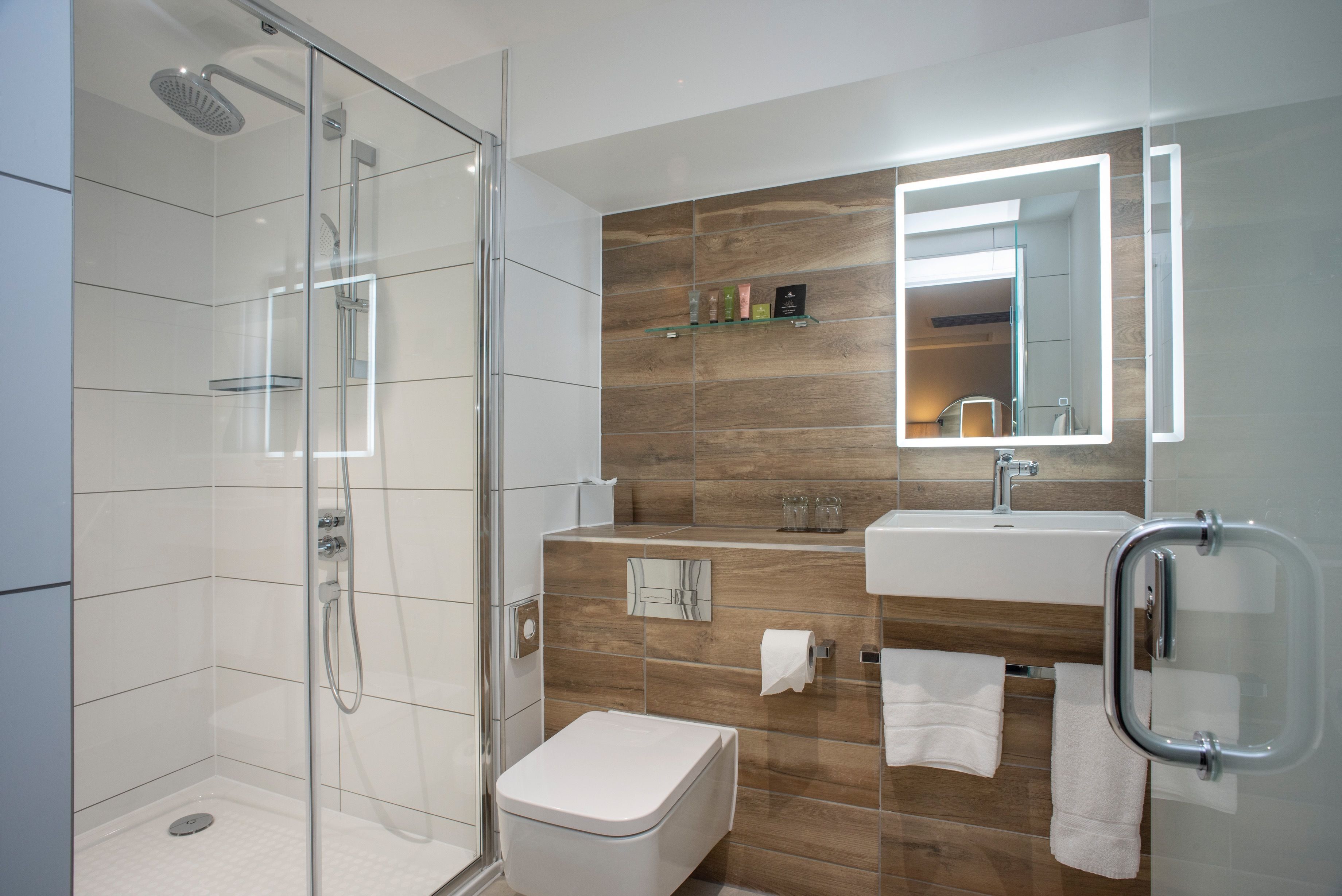 Een moderne badkamer met een douchecabine van glas, een wit toilet, een wastafel met spiegel en een handgreep.