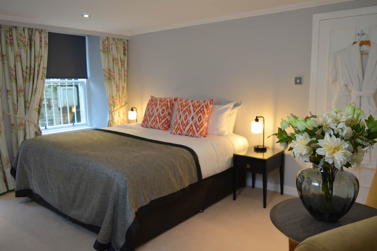A bedroom with a bed, bedside lamps, a vase with flowers, and a robe hanging on a door.