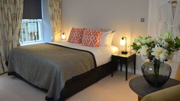 A bedroom with a bed, bedside lamps, a vase with flowers, and a robe hanging on a door.