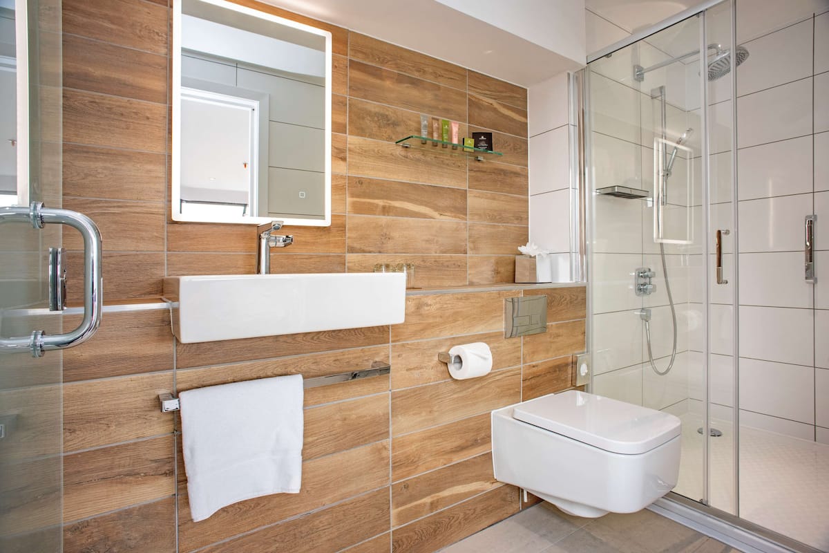 A modern bathroom with a wooden wall, a glass shower enclosure, a white sink, and a toilet.