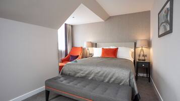 Una habitación de hotel moderna con una cama grande, dos mesitas de noche, un banco y una ventana con cortinas.