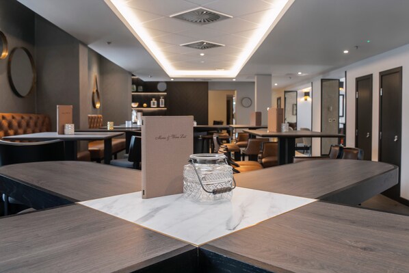 Un moderno vestíbulo de hotel con una mesa central de mármol, un tarro de vidrio y un atril para menús.