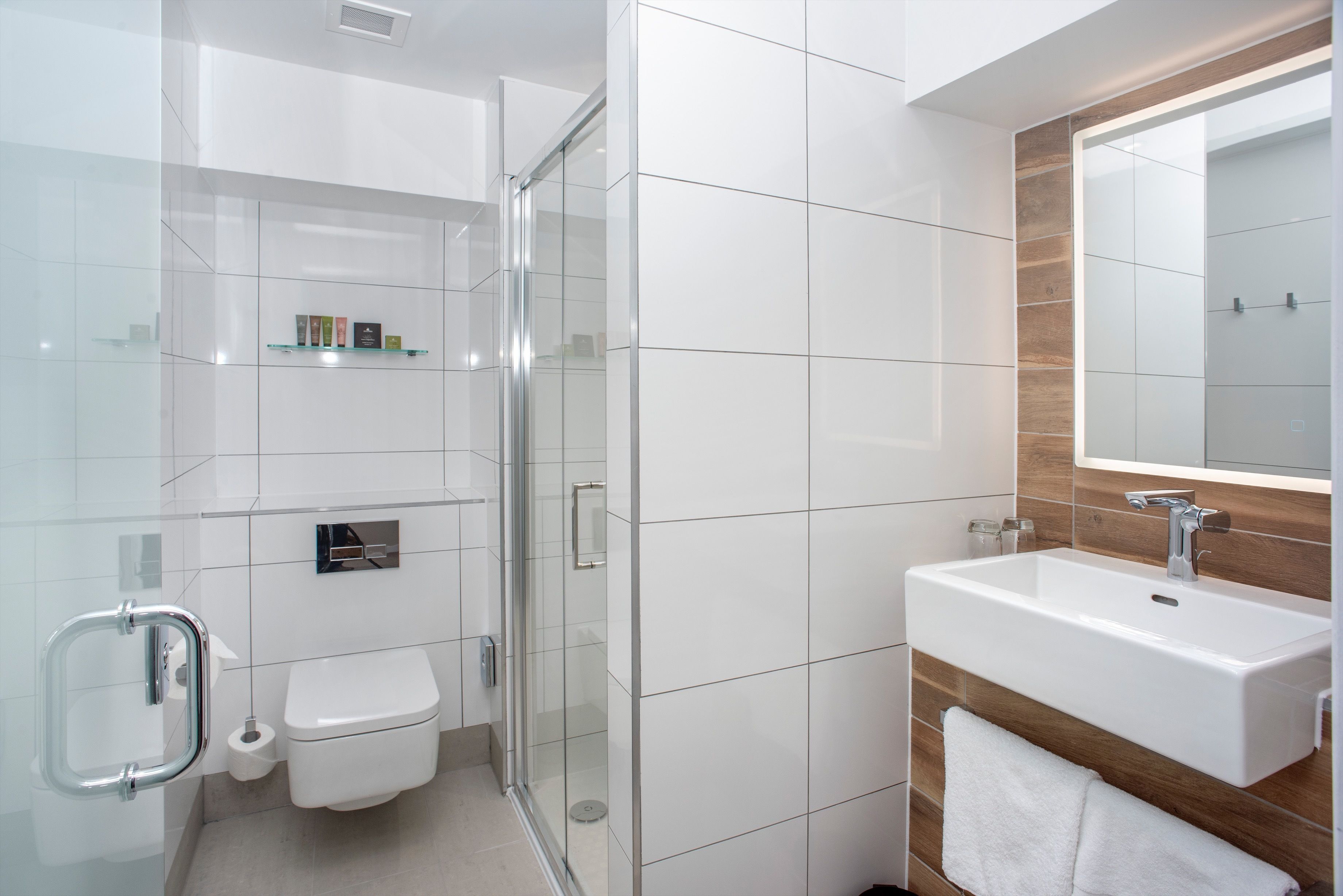 A modern bathroom with a glass shower enclosure, a white sink, and a wooden vanity.