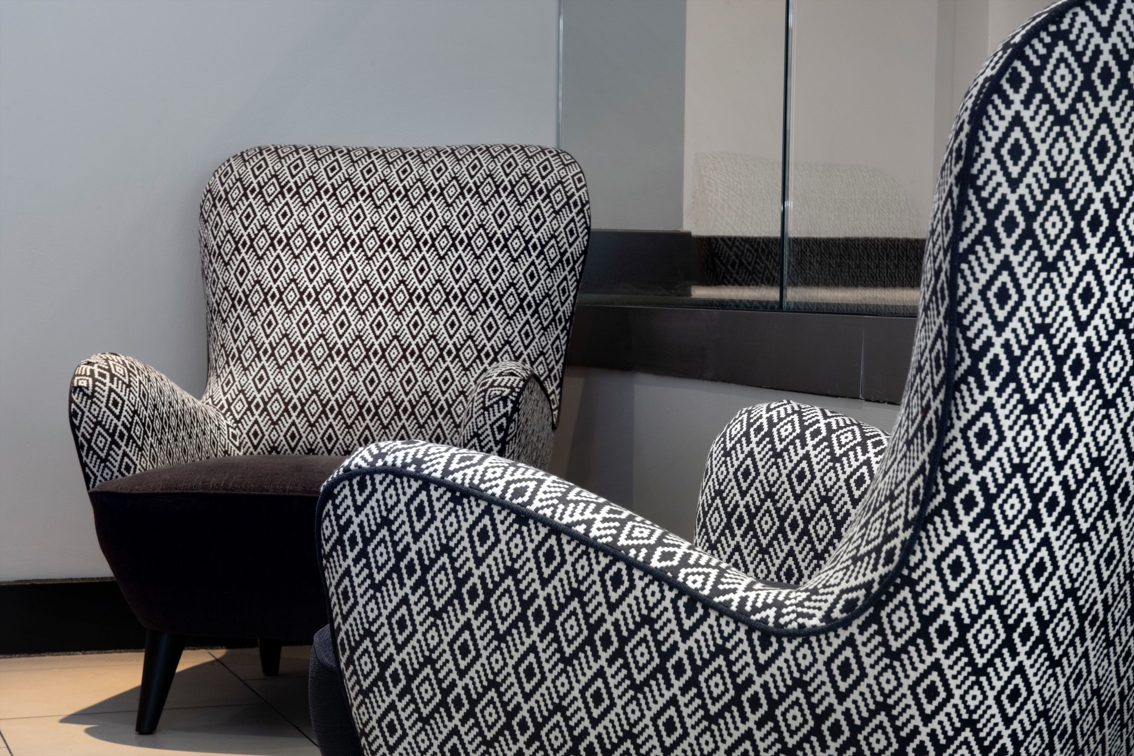 A modern chair with a geometric pattern, positioned in a room with a plain wall and a window.