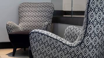A modern chair with a geometric pattern, positioned in a room with a plain wall and a window.