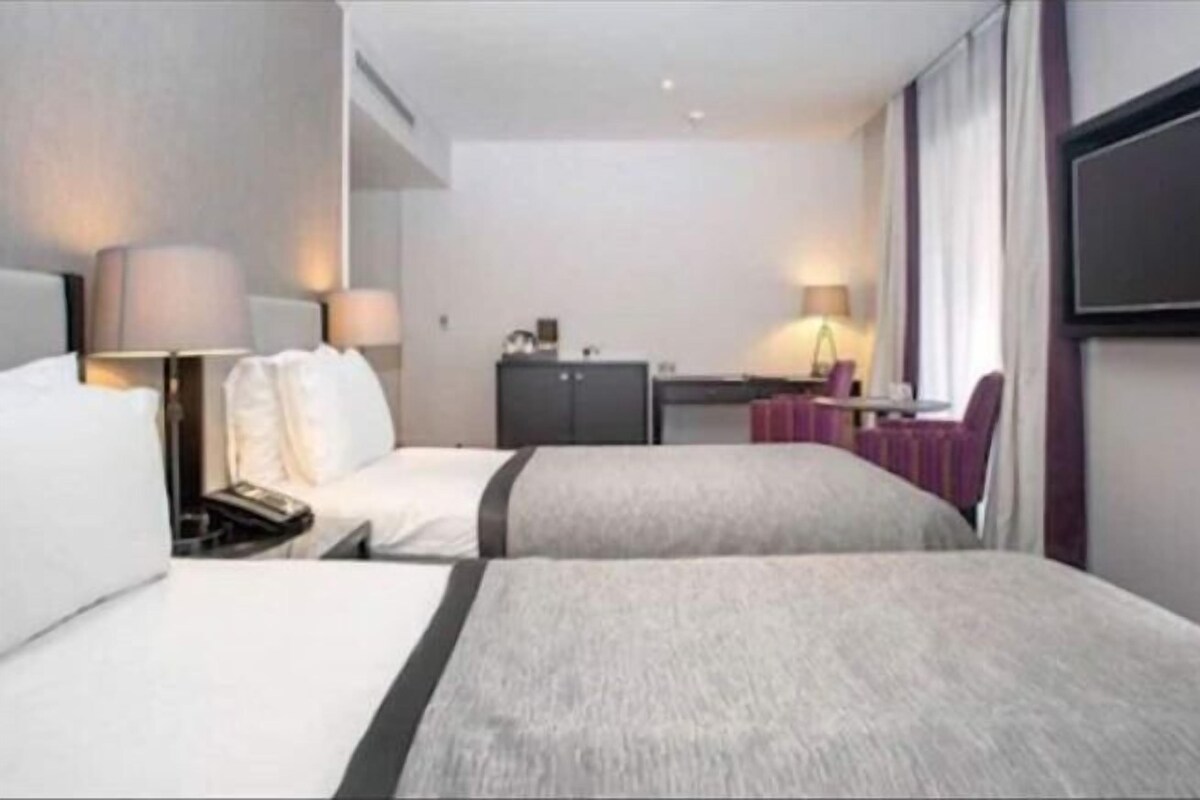 A hotel room with two beds, a desk, a chair, and a TV mounted on the wall.