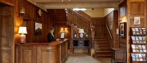 A wooden reception desk with a chandelier, a staircase, and a display of brochures.