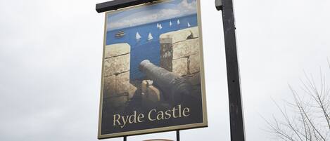 A sign for Ryde Castle pub with a coastal scene and a flag.