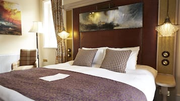 Habitación de hotel con una cama grande, cabecera con pintura, mesita de noche con lámpara y vistas al exterior.