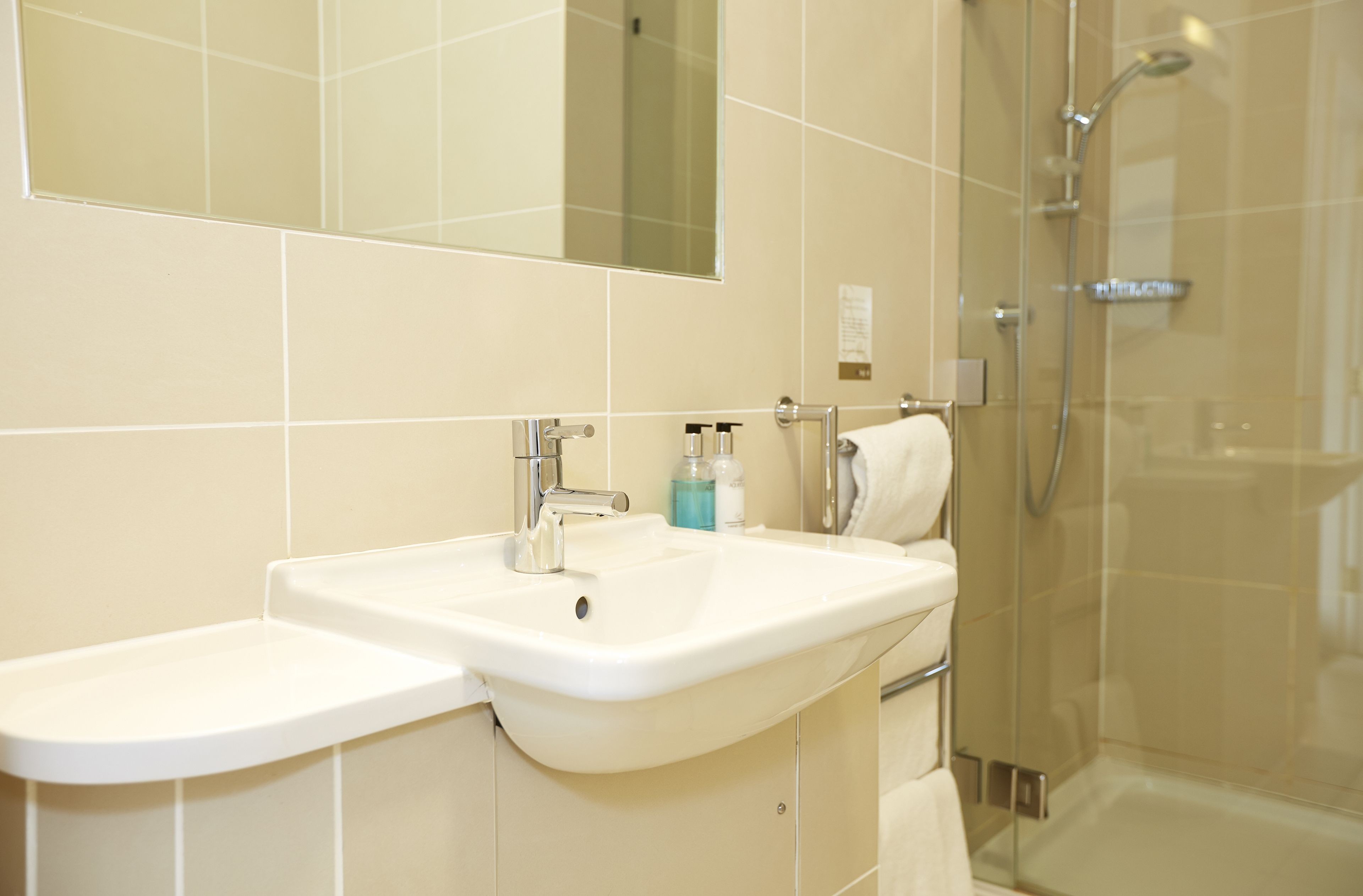Un baño con lavamanos blanco, un espejo y cabina de ducha con mampara de vidrio.