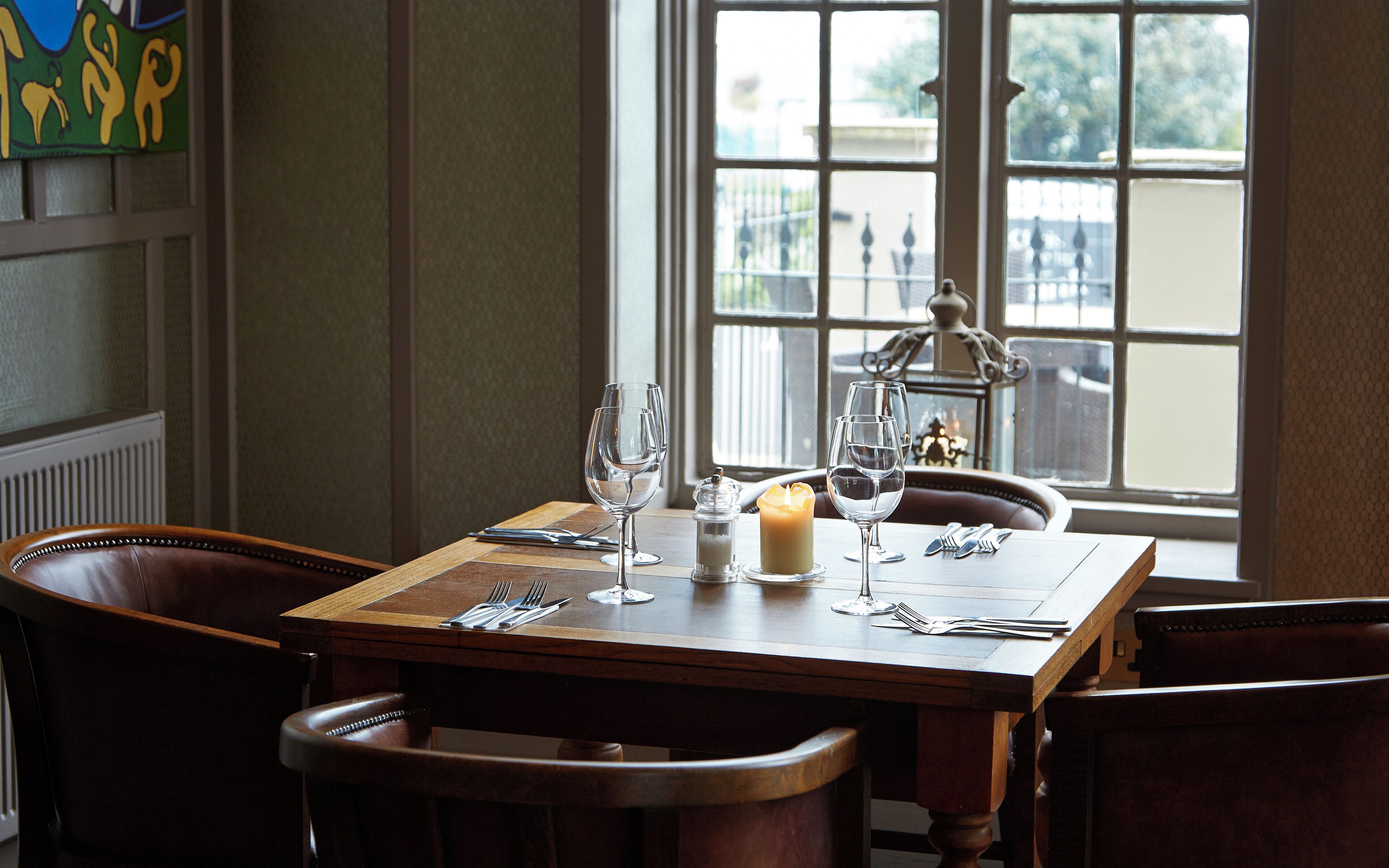 A dining table set with wine glasses, a candle, and cutlery.