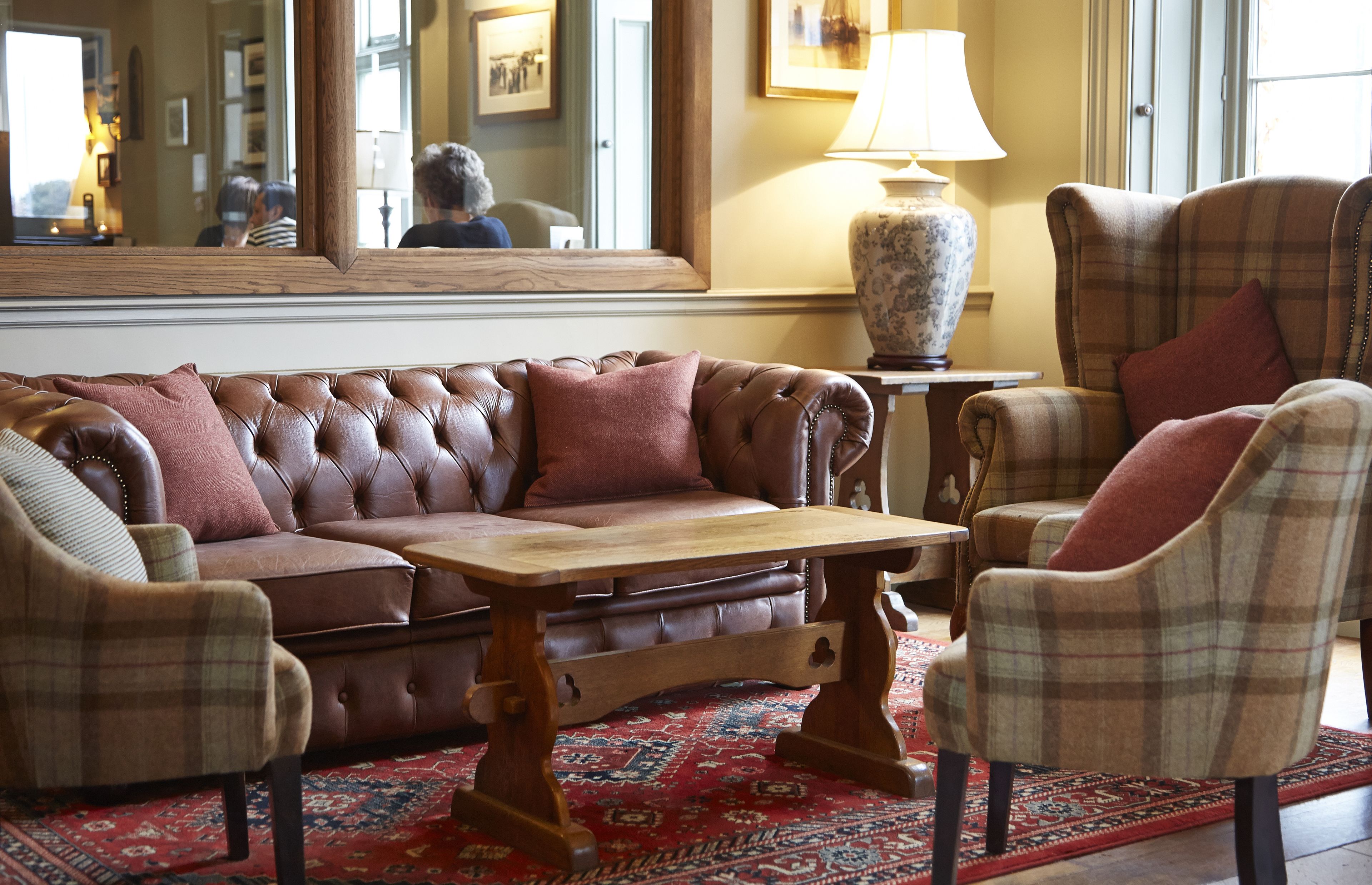 A living room with a brown leather sofa, plaid armchairs, a wooden coffee table, and a patterned rug.