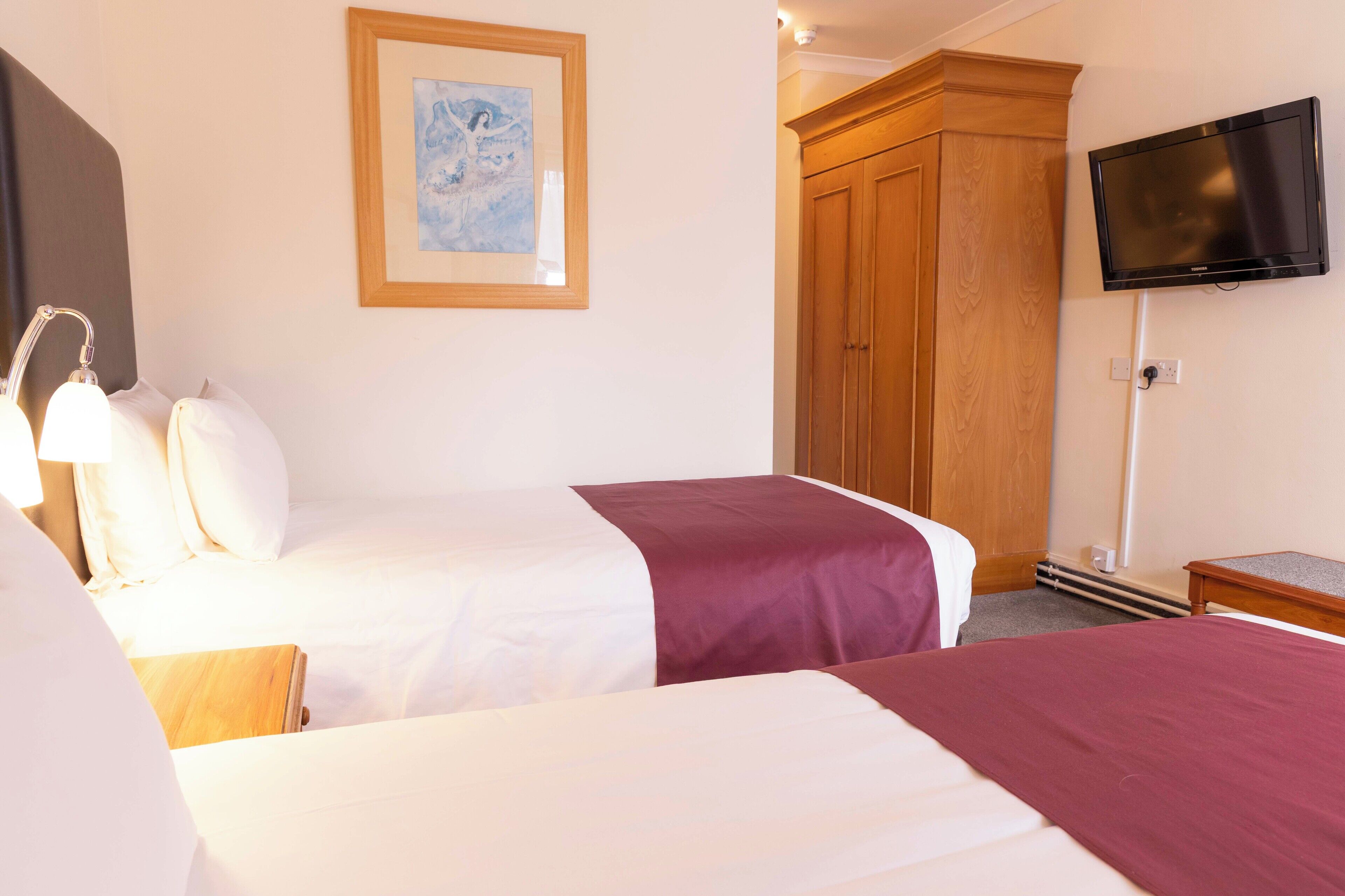 Een hotelkamer met twee bedden, een houten garderobe, een televisie en een ingelijste foto aan de muur.