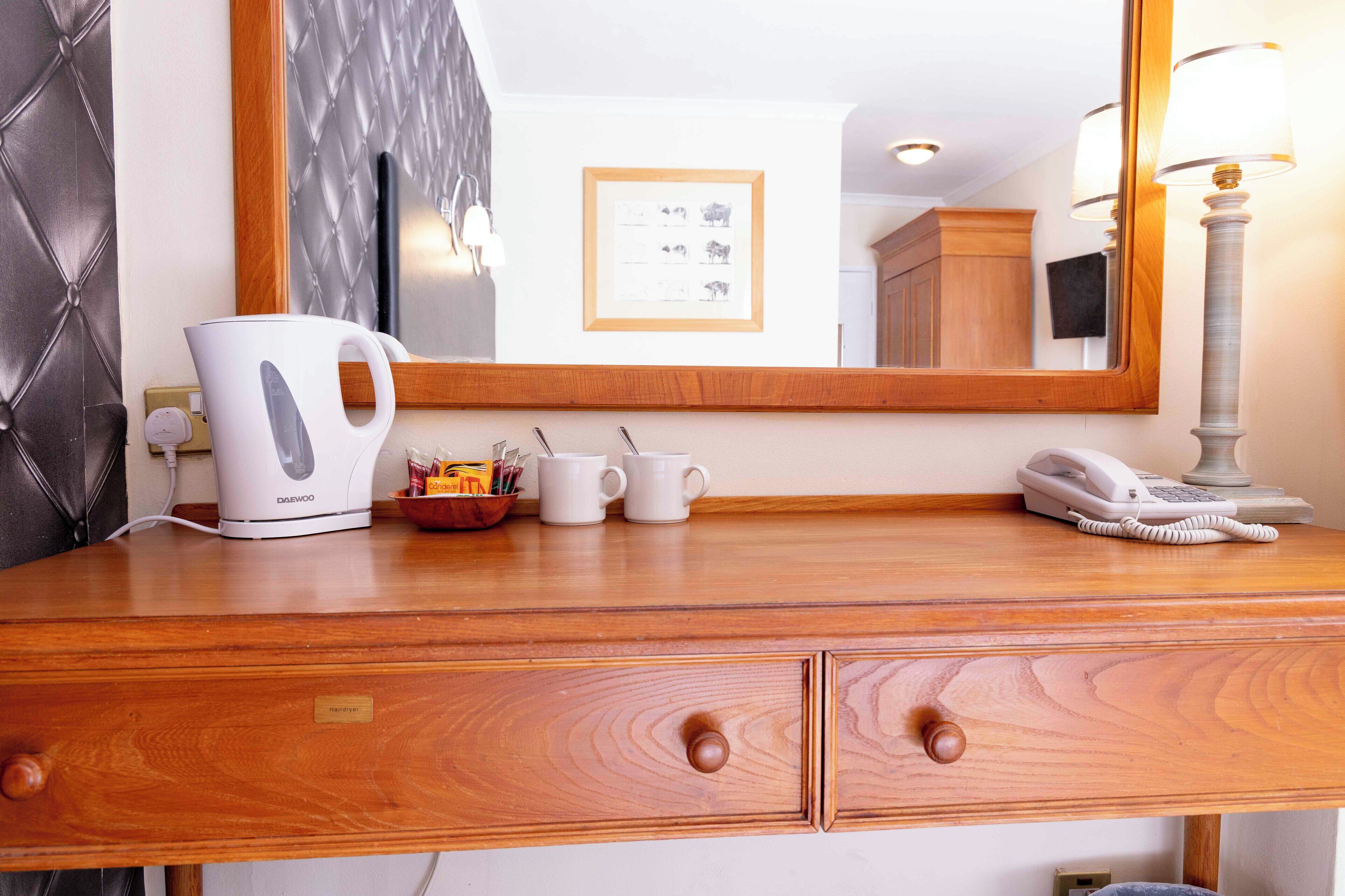 A wooden dresser with a white electric kettle, two white mugs, a small bowl with utensils, and a white telephone.