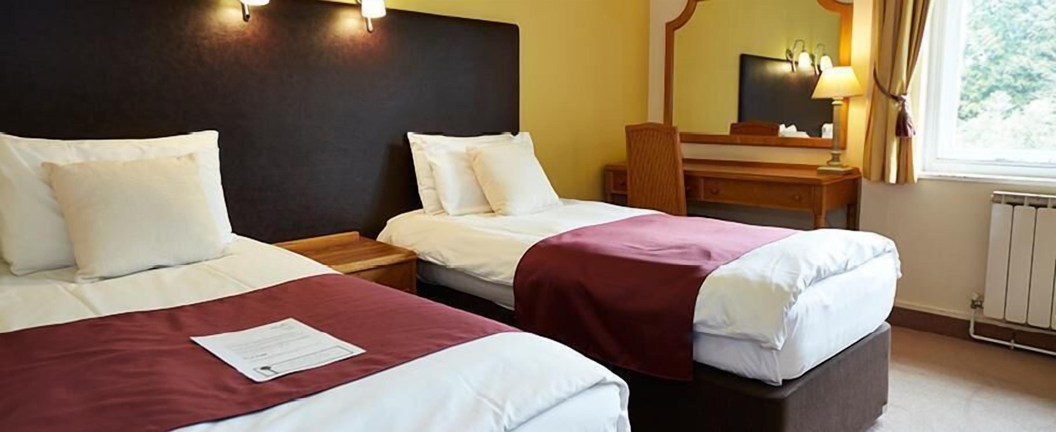 Habitación de hotel con dos camas, un escritorio y un espejo.