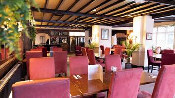 Un restaurant avec des chaises à revêtement rouge, des tables en bois et un coin bar doté d’étagères à vin.