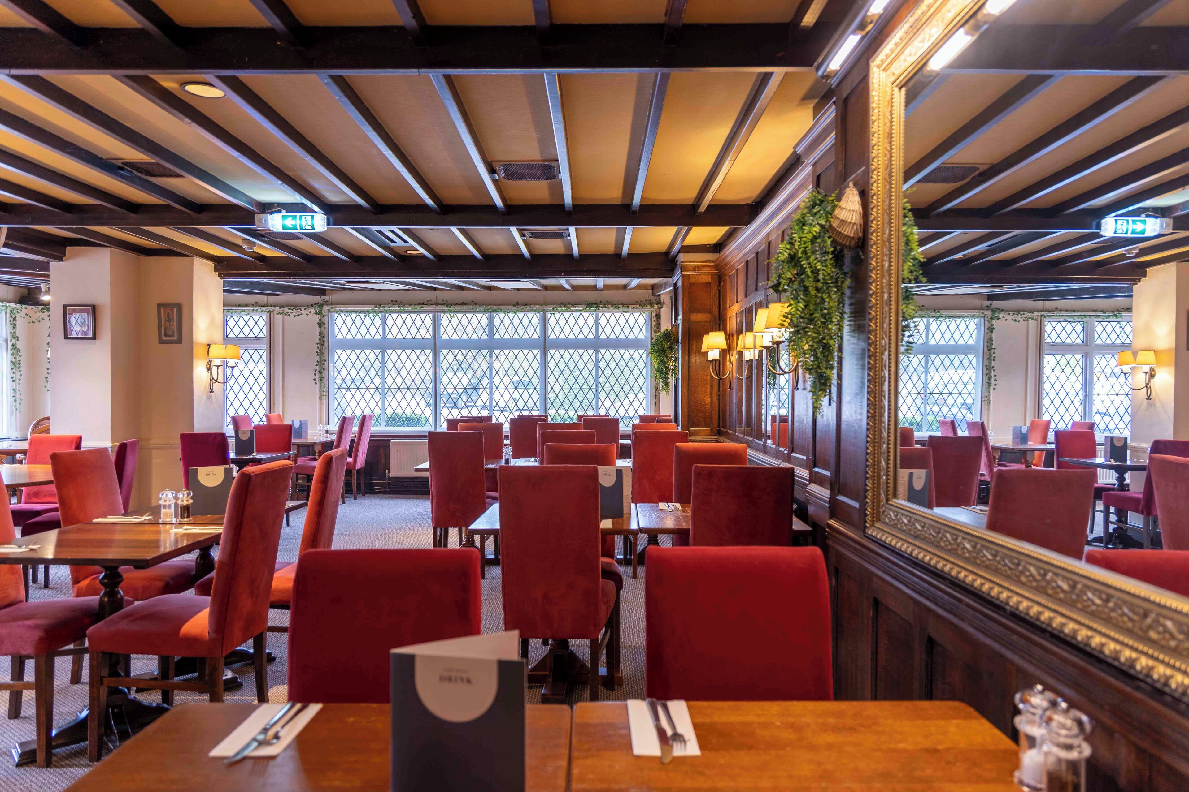 A restaurant with red upholstered chairs, wooden tables, and a large mirror on the wall.