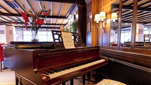 Un piano de cola con partituras en una habitación de paredes de madera y un espejo grande que refleja el ambiente.