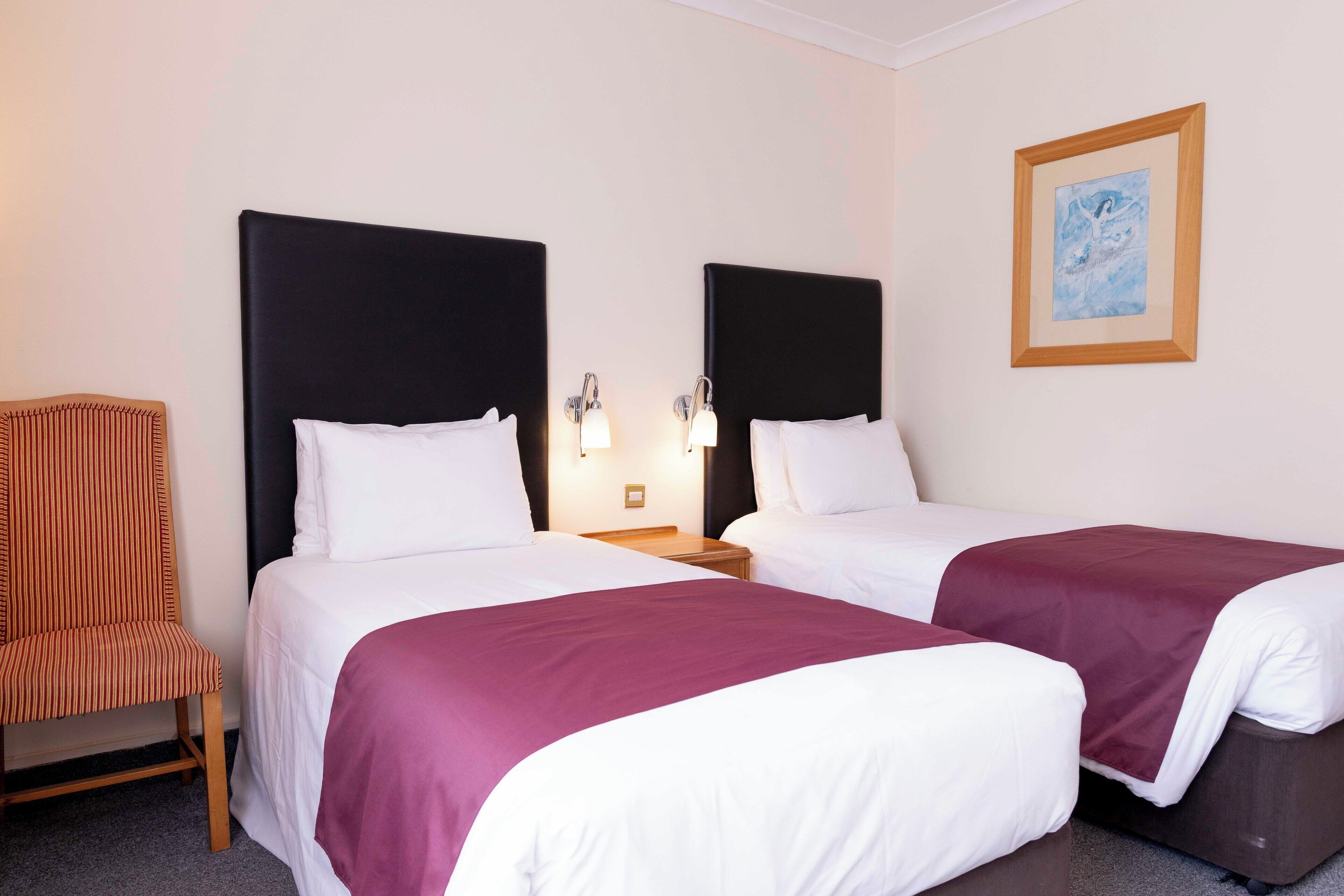 A hotel room with two beds, a chair, and a framed picture on the wall.