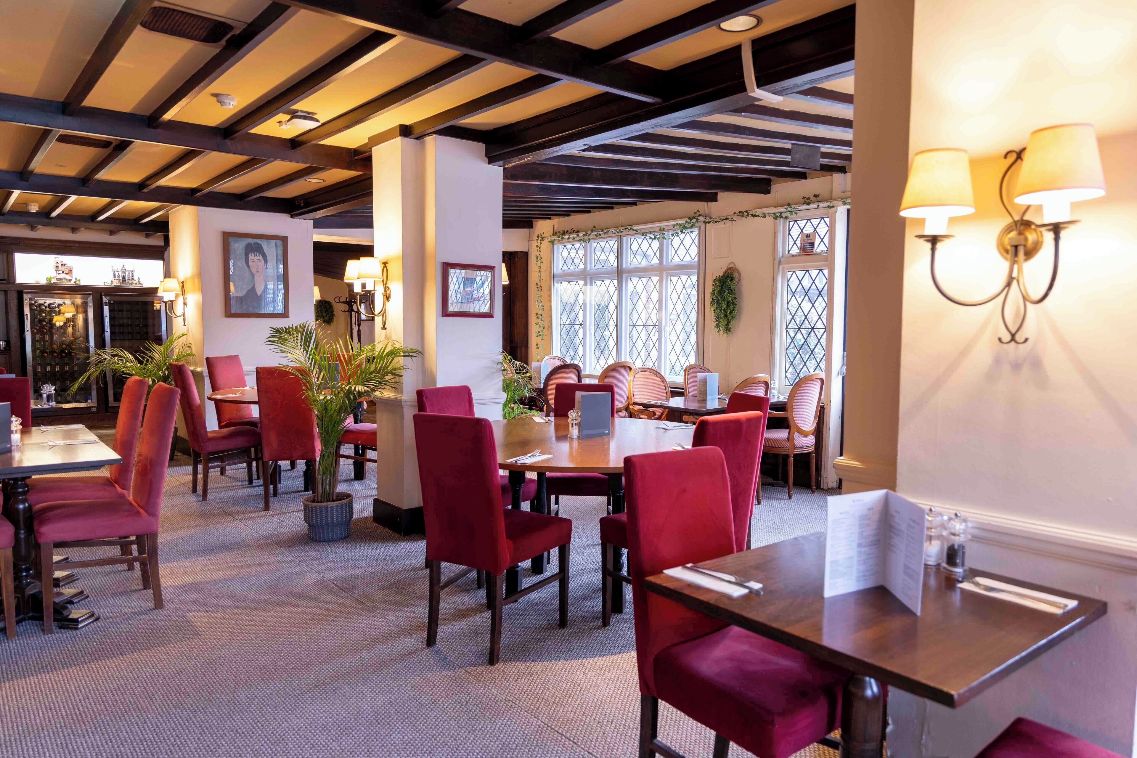 A restaurant with red upholstered chairs, wooden tables, and a high ceiling with exposed beams.