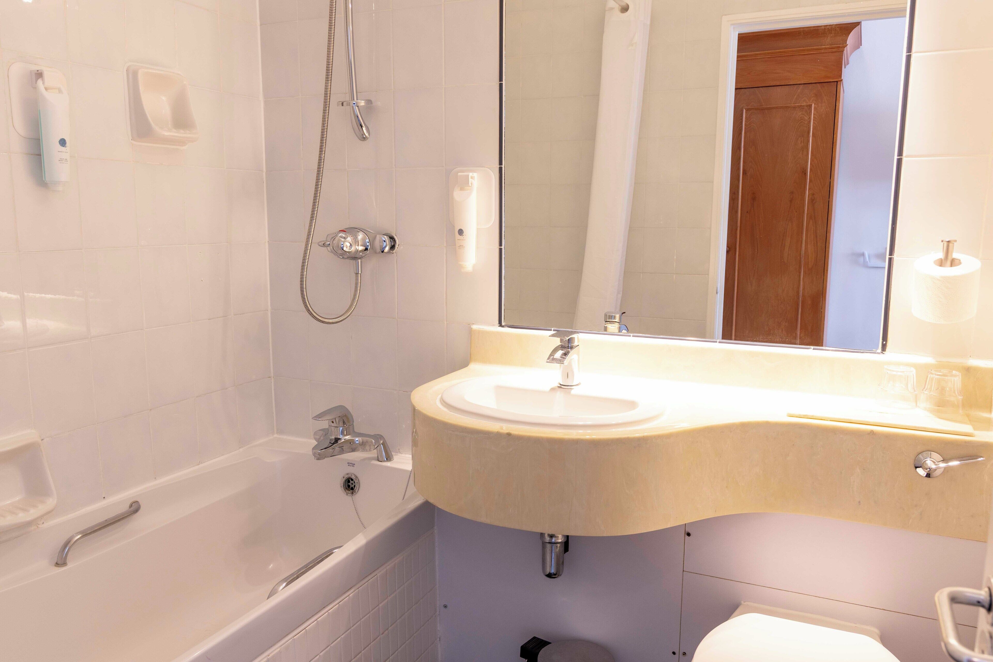 Un baño con bañera, lavamanos, espejo e inodoro.