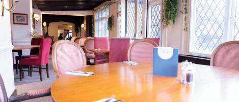 A restaurant with round tables, red upholstered chairs, and a wooden ceiling.