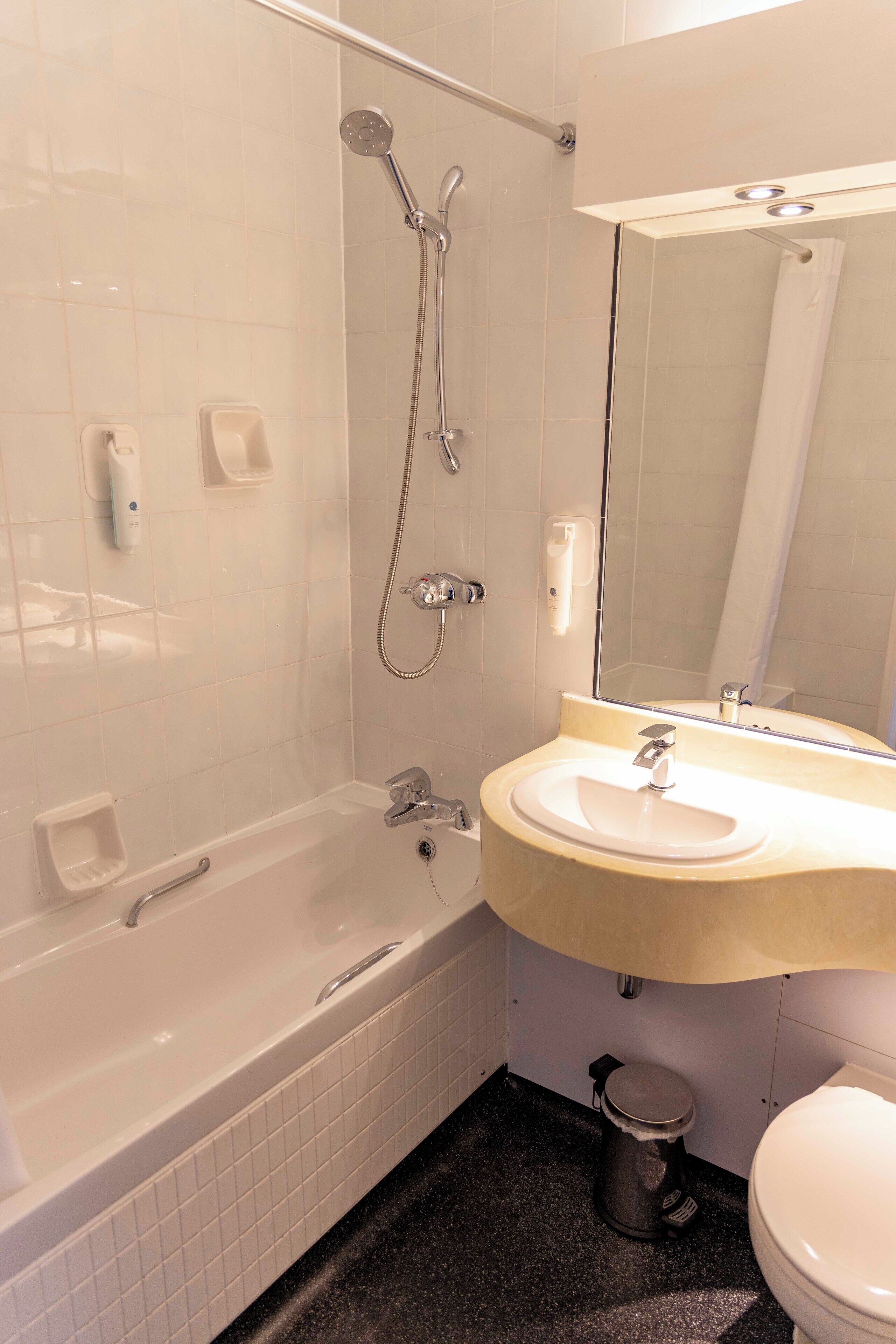 Et badeværelse med badekar, vask, toilet og bruser.