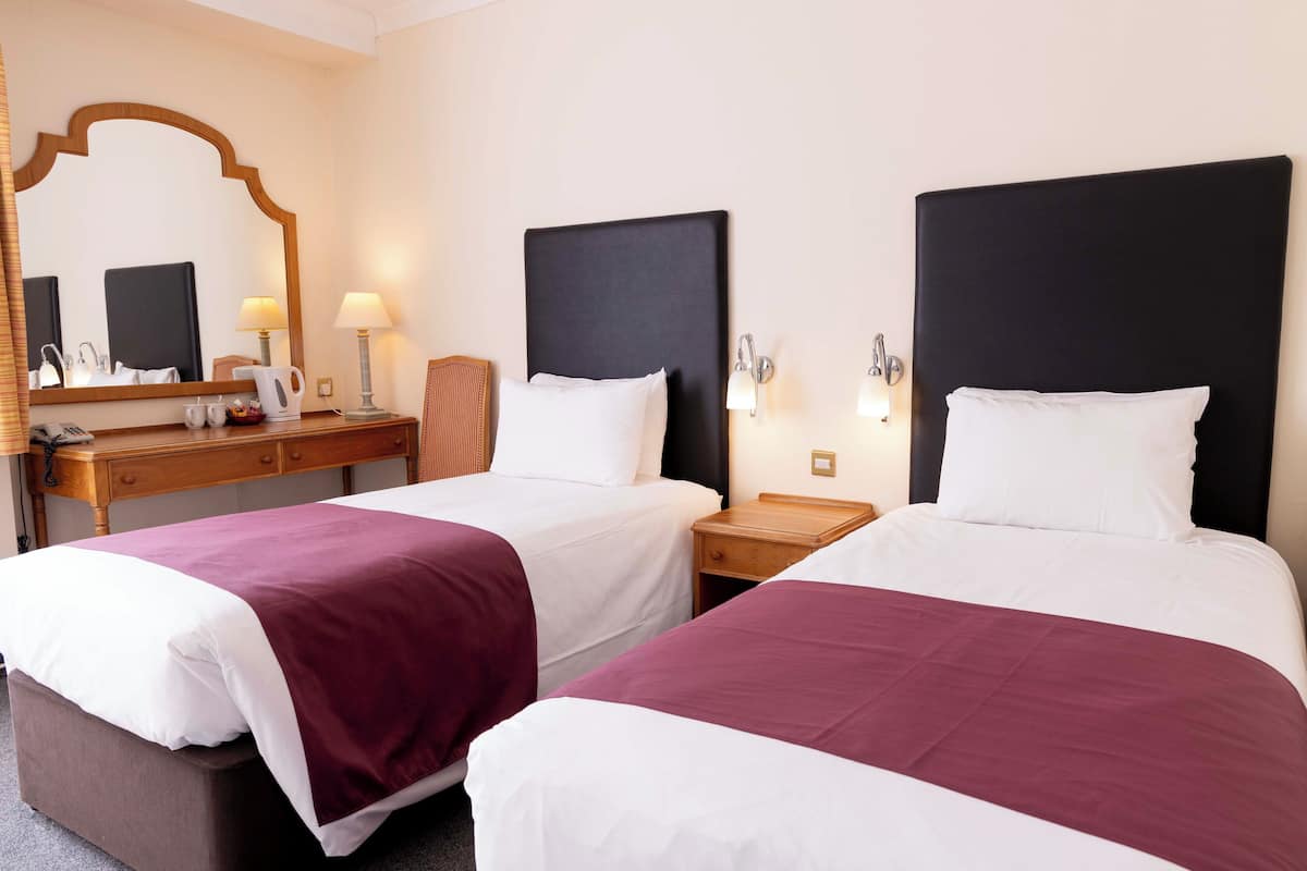 Une chambre d’hôtel avec deux lits, un bureau en bois, un miroir et des lampes de chevet.