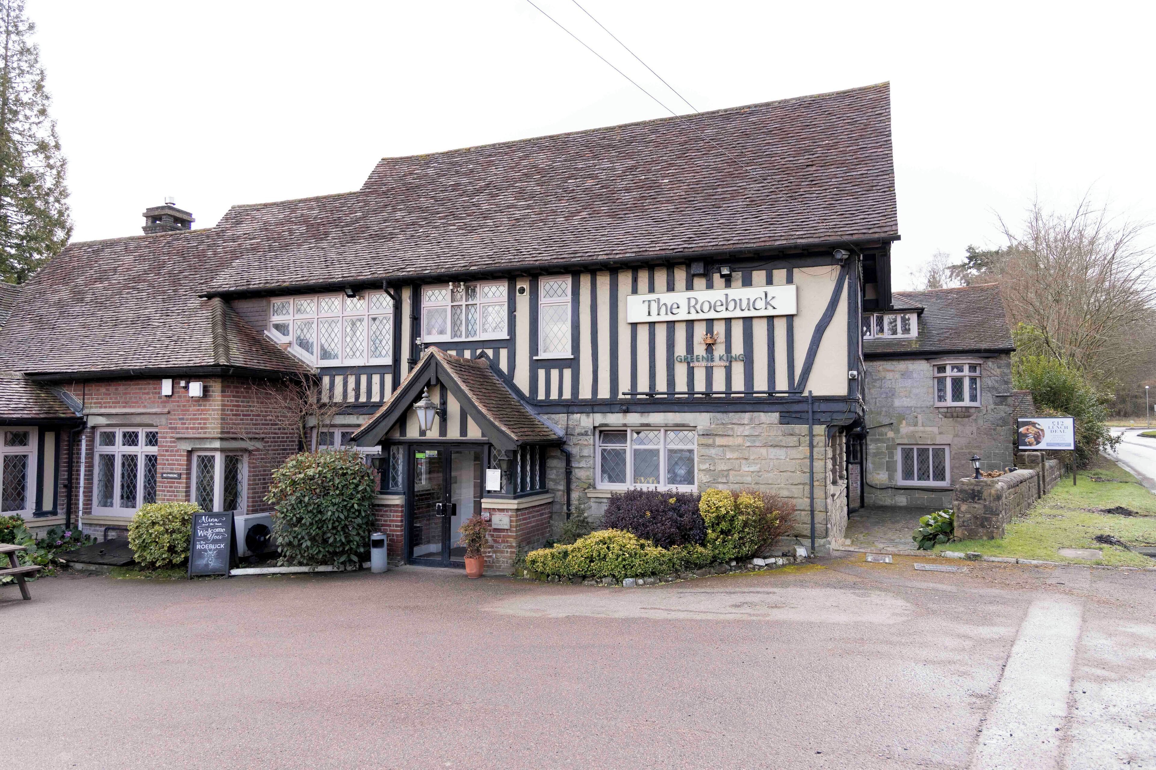 A traditional half-timbered building named "The Roebuck" with a stone facade and a signboard.