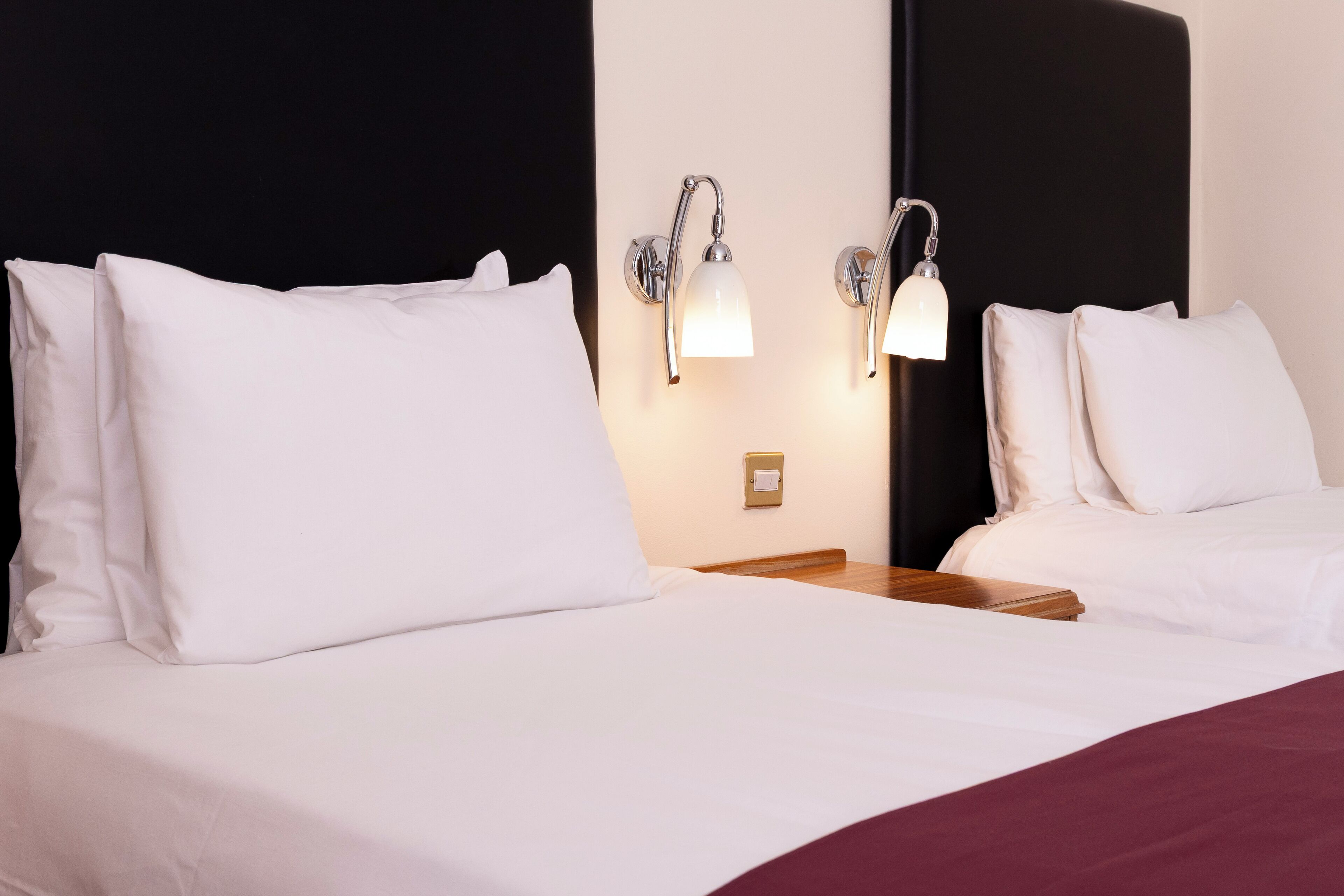 Habitació d'hotel amb dos llits, roba de llit blanca, una tauleta de nit de fusta i aplics murals.
