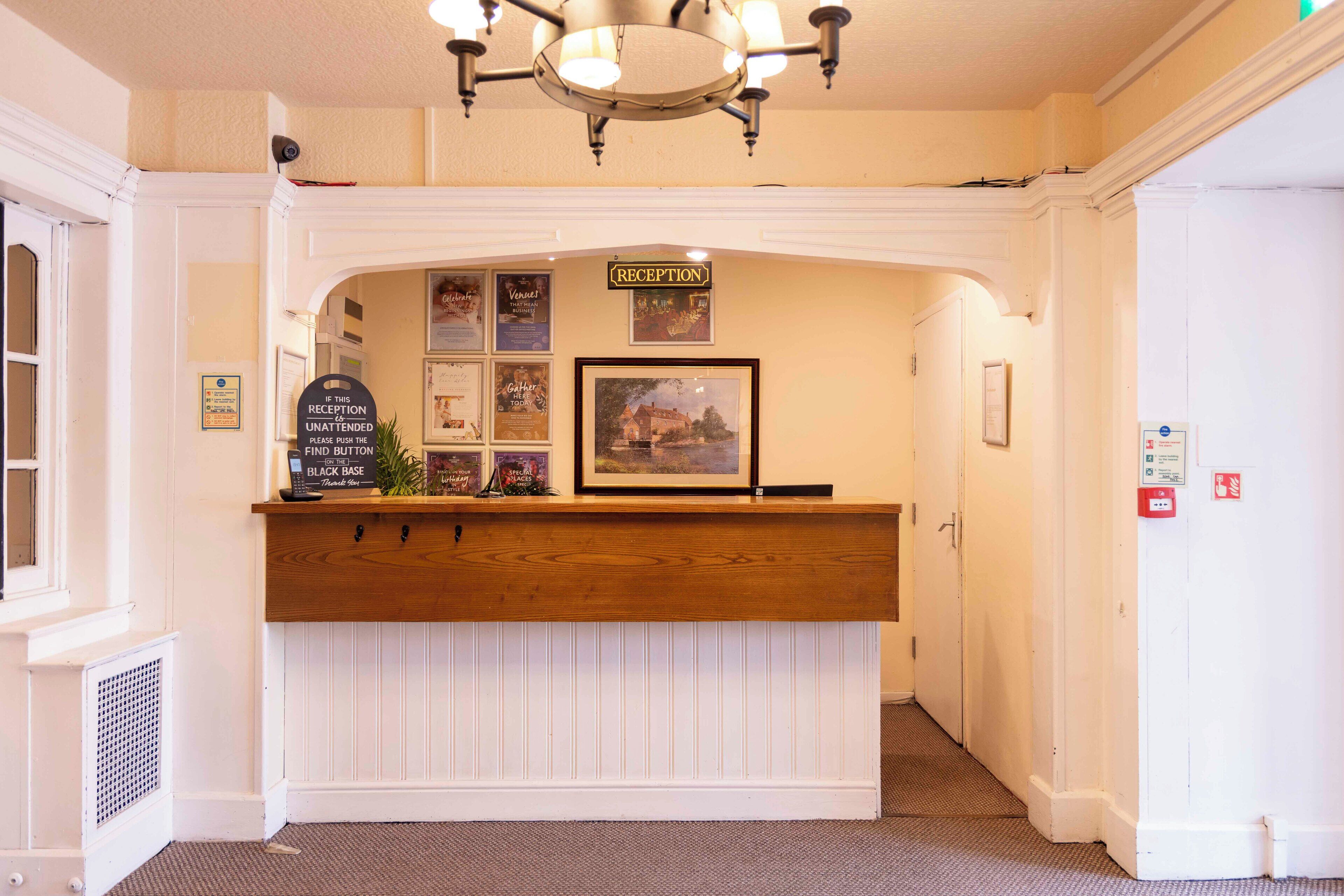 A reception desk with a sign indicating 'RECEPTION', a framed picture above it, and a sign with instructions for finding the black base.
