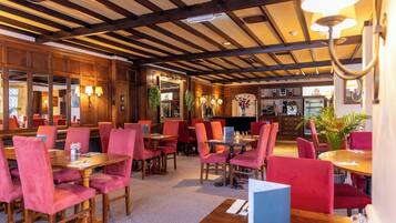A restaurant with wooden beams and red upholstered chairs. Tables are set with white tablecloths and centerpieces.