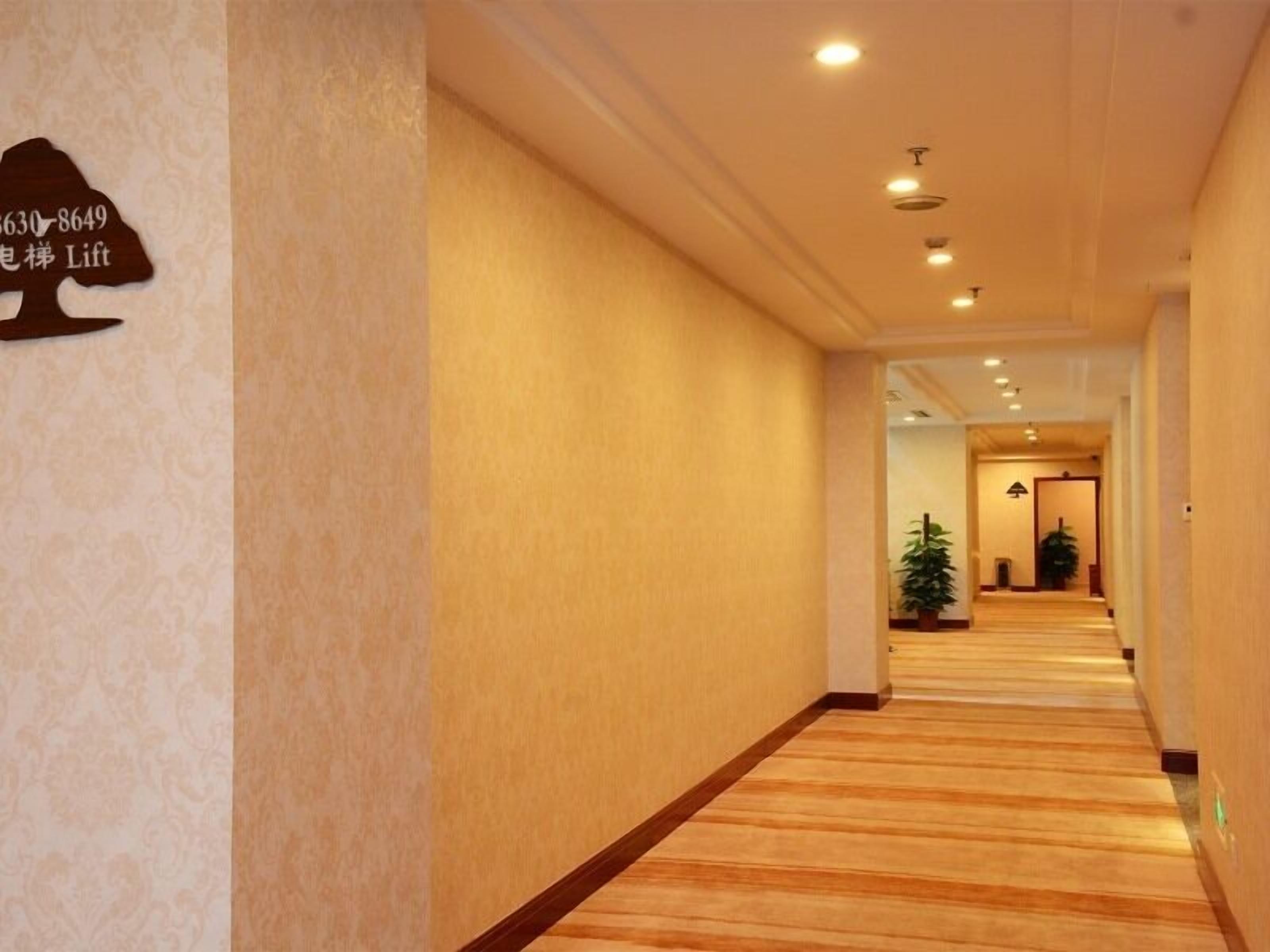 A hotel corridor with wooden flooring, a sign with a phone number, and a potted plant.