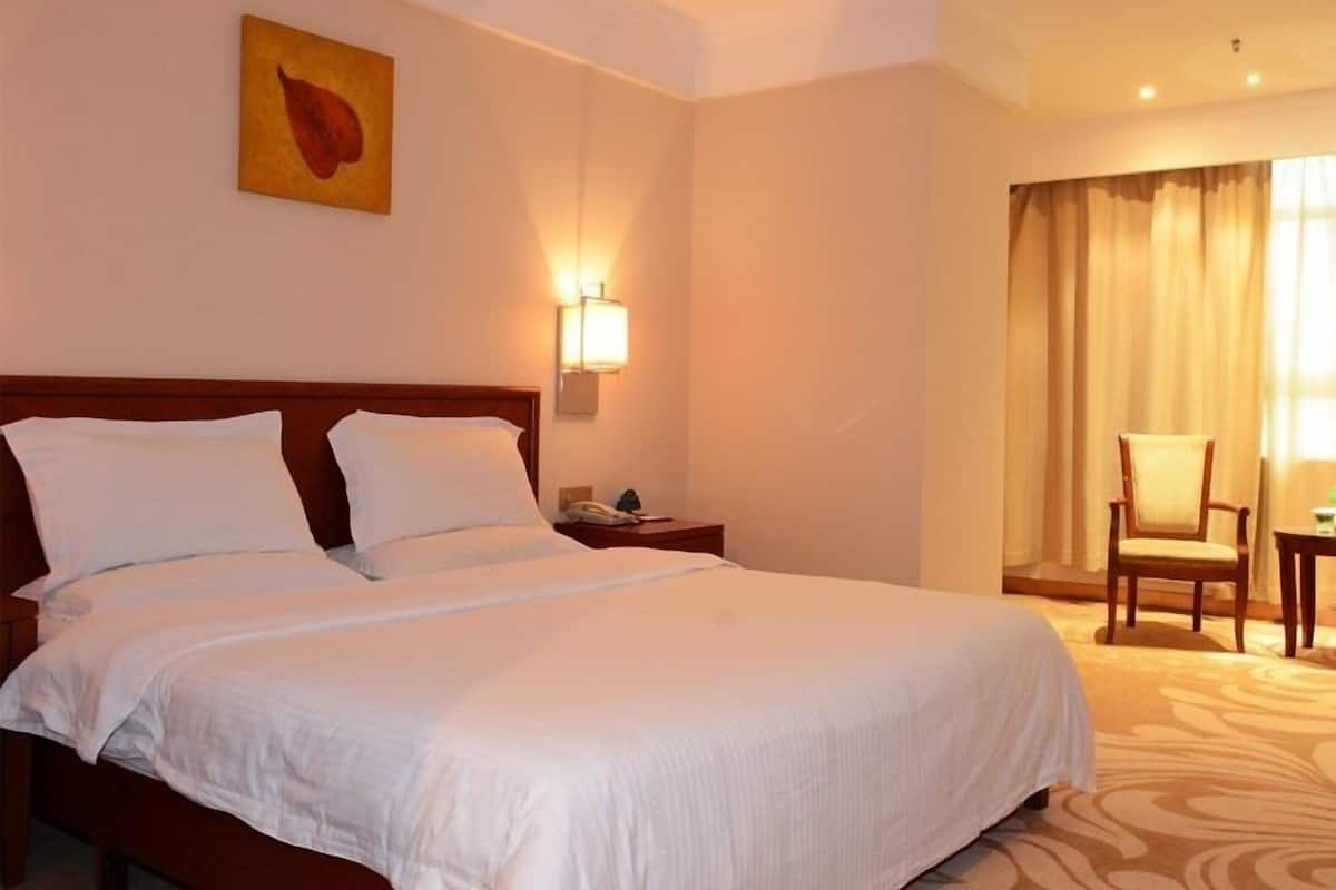 Una habitación de hotel con una cama grande, una mesita de noche, una lámpara, una silla y un cuadro en la pared.