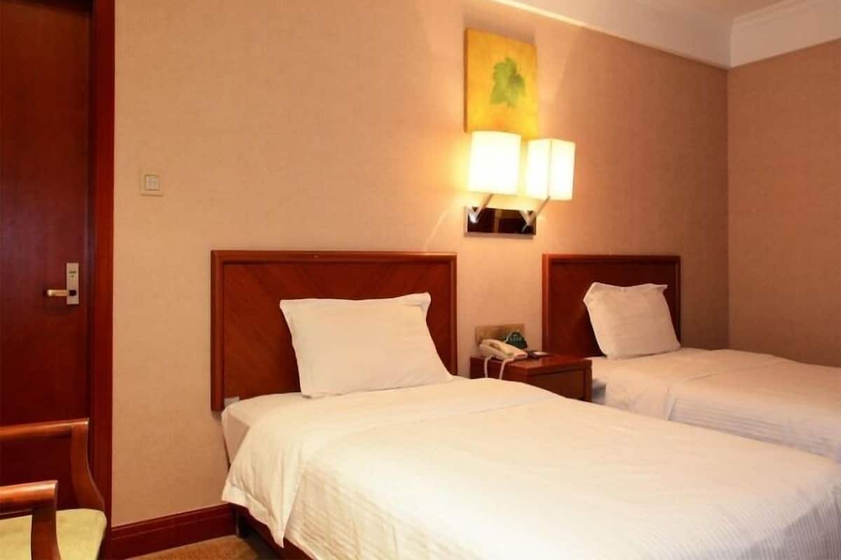 Habitación de hotel con dos camas individuales, una puerta de madera, una lámpara fijada a la pared y una mesita de noche pequeña con un teléfono.