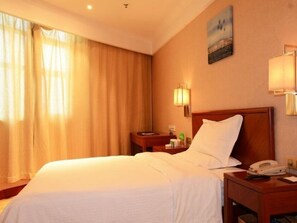 Una camera d'albergo con un letto grande, un comodino con una lampada, un telefono e un quadro appeso al muro.