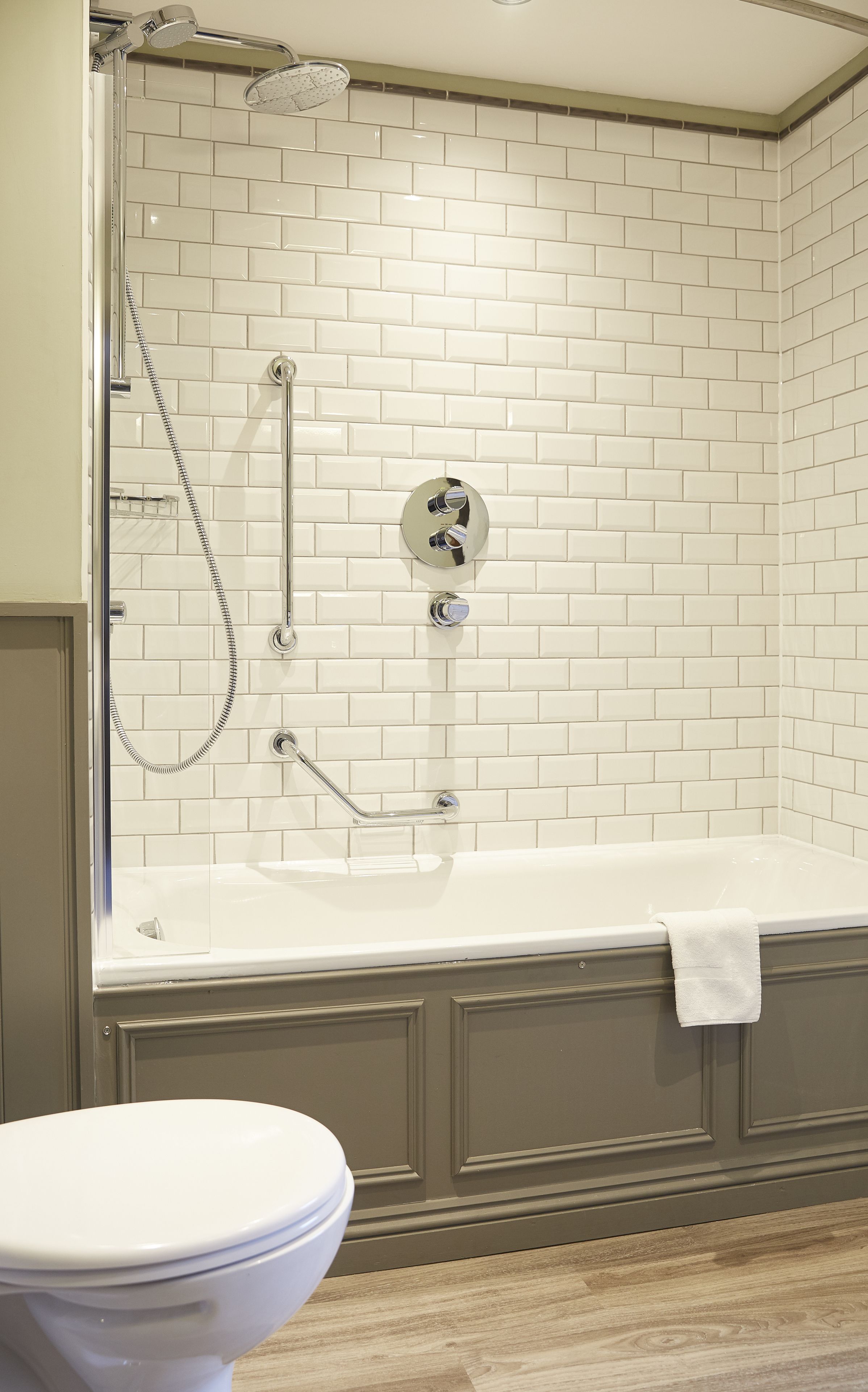 A bathroom with a white-tiled shower enclosure, a bathtub with a towel, and a toilet.