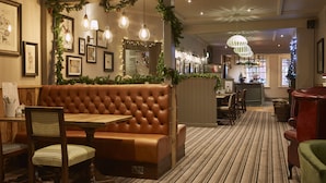 A cozy restaurant with a tufted leather booth, wooden chairs, and a striped carpet. - Swan Hotel by Greene King Inns (Alton)