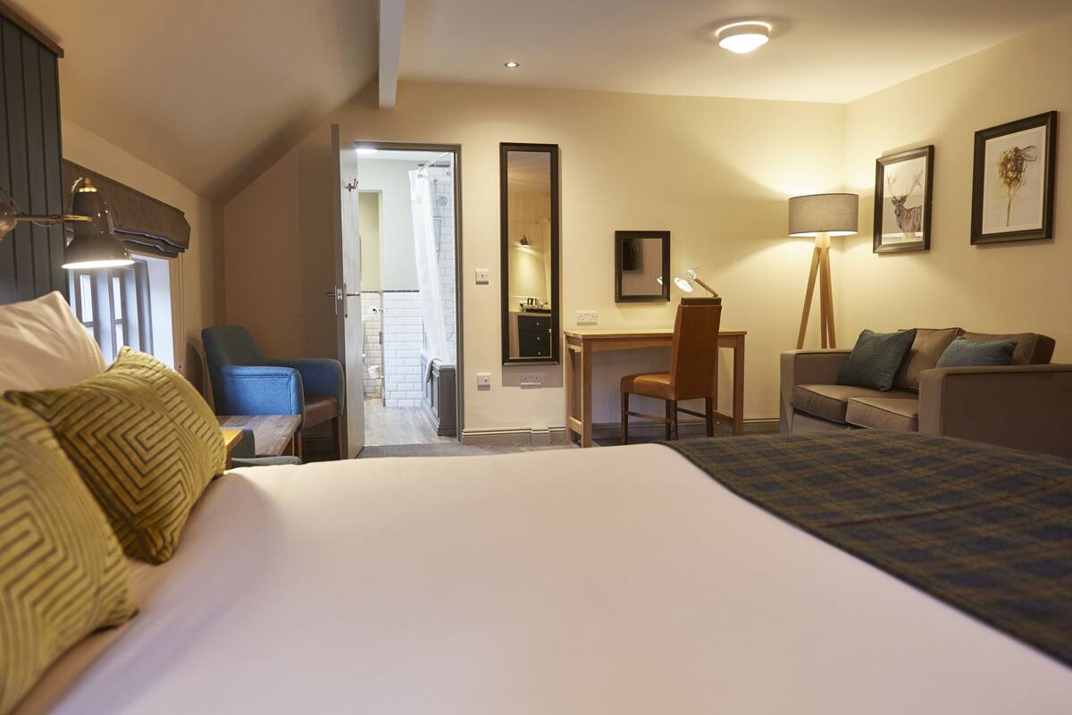 A hotel room with a bed, a desk, a chair, a sofa, a lamp, and a mirror.