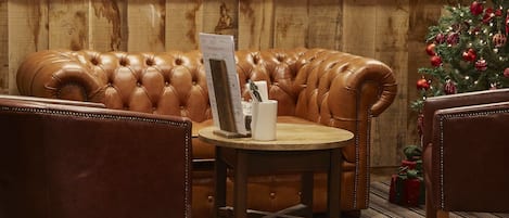 A leather sofa with a menu stand, two chairs, a small round table, and a Christmas tree with ornaments.