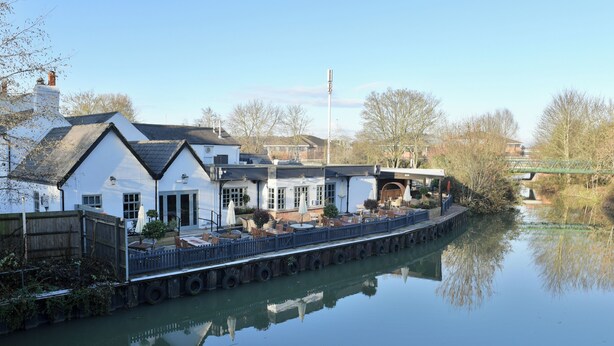 A riverside building with a dock extending into the water, featuring outdoor seating and a covered area. - Swan Hotel by Greene King Inns (Alton)