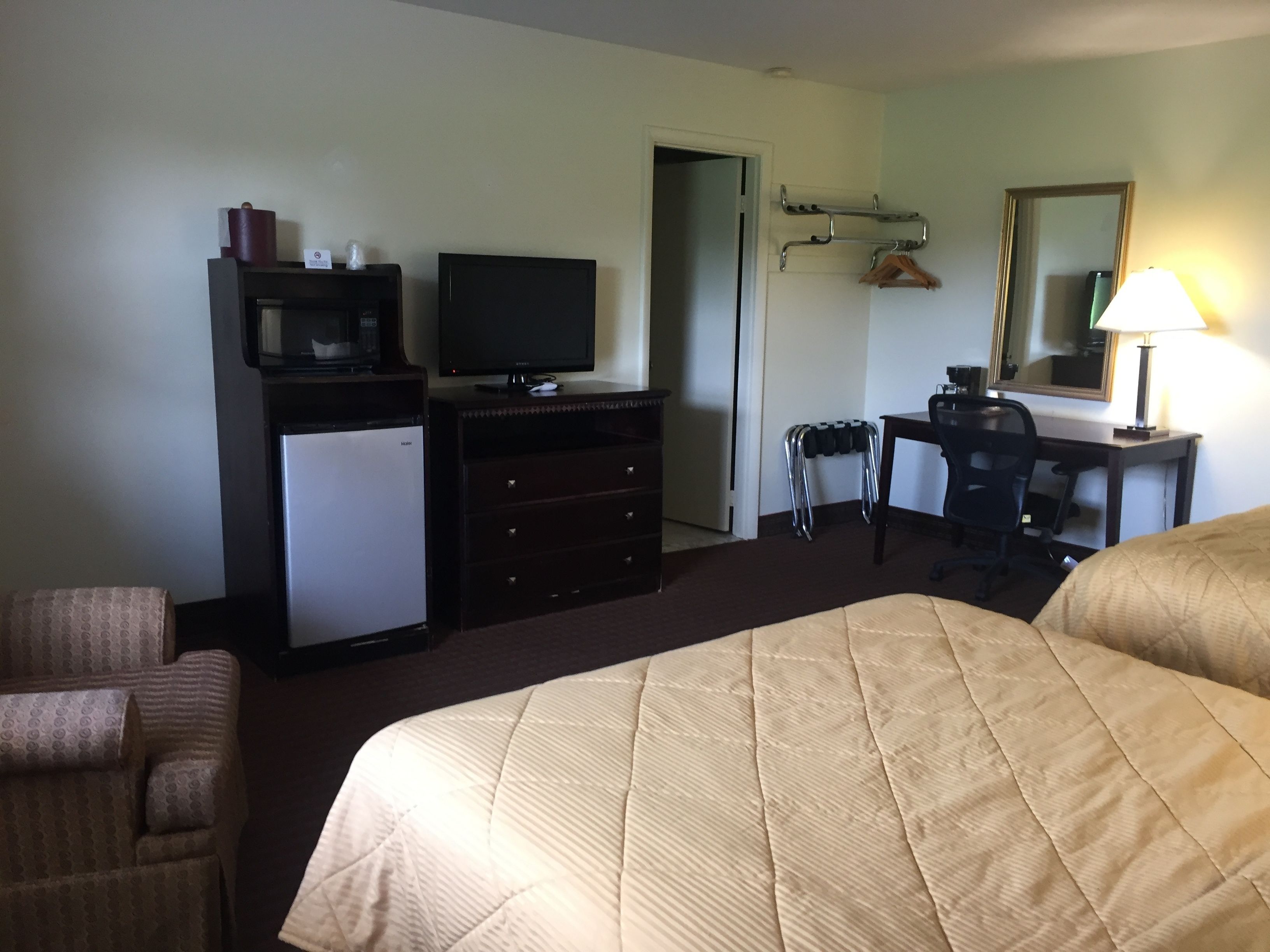 A hotel room with a bed, a desk with a chair, a television, a small refrigerator, and a wardrobe.