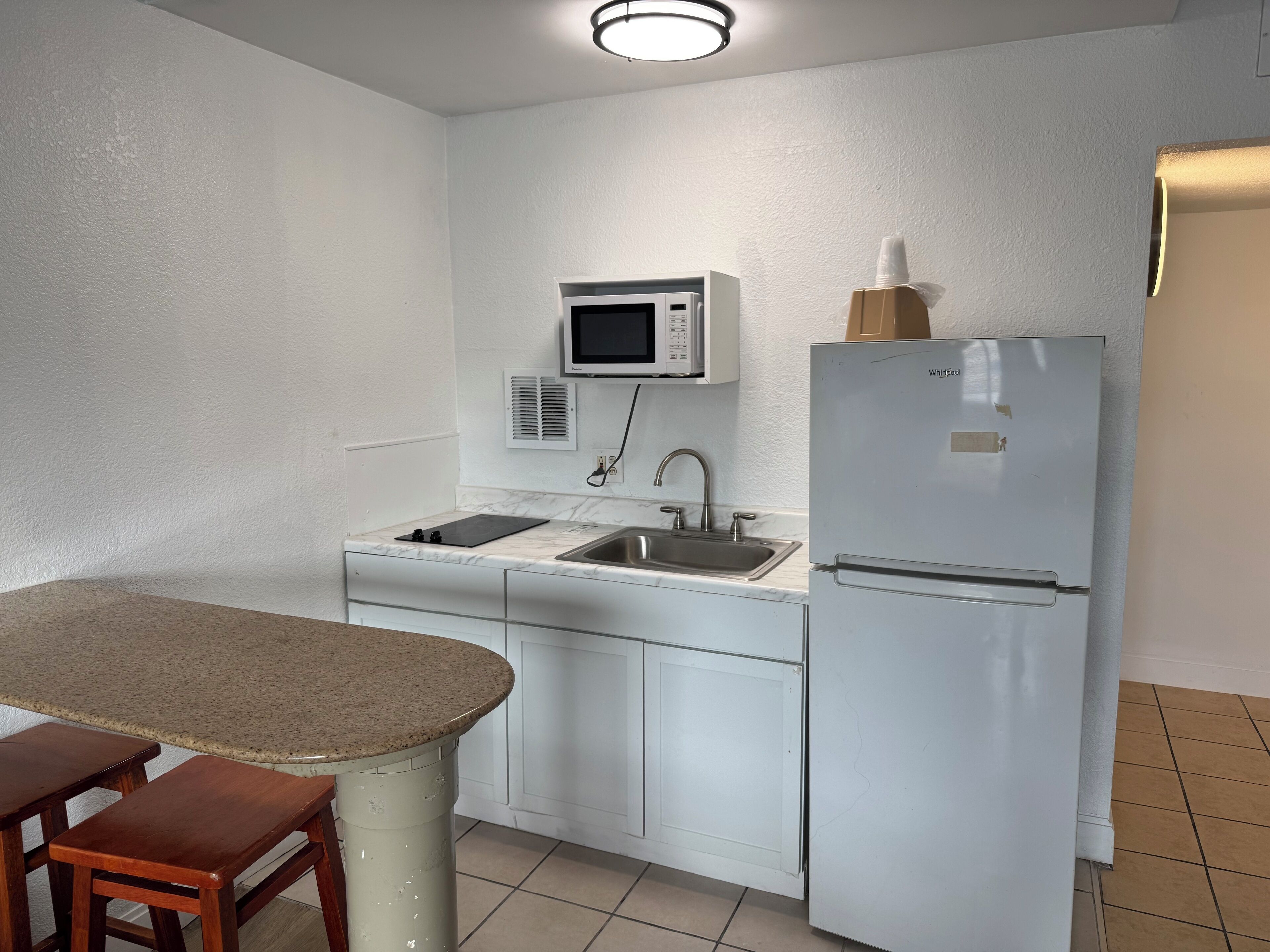 A compact kitchen with white cabinets, a stainless steel sink, a microwave, and a refrigerator.