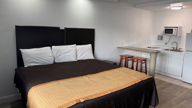 A modern hotel room with a large bed, a small kitchenette, and a white textured wall. - Belmont Inn And Suites (Virginia Beach)
