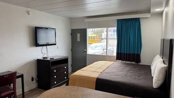 Habitación de hotel con cama, escritorio, televisor, armario y ventana con cortinas.